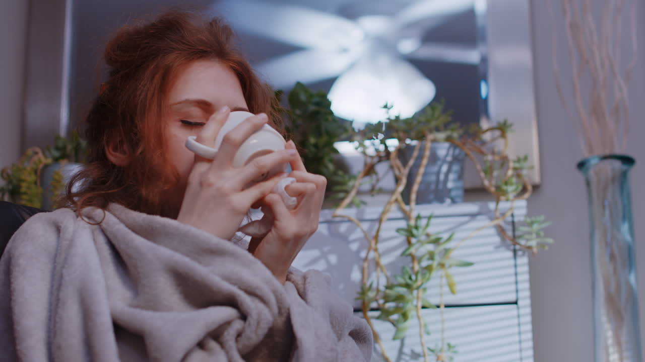 백인 여성이 집에서 아프고, 회복하고, 기분이 좋아지고, 컵에서 마시고 있습니다.