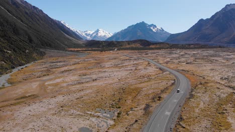 scenic drone shot of a car driving into the mountains through beautiful scenery on a clear sunny day in 4k