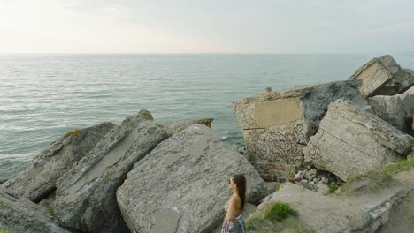 vista aérea de una hermosa joven caucásica romántica en un vestido largo en la playa de arena blanca con viejas ruinas, noche soleada de verano, puesta de sol, hora dorada, tiro de dron ancho avanzando