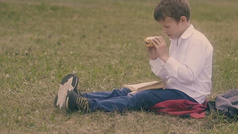 un niño de camisa blanca disfruta de una hamburguesa sentado en el patio verde