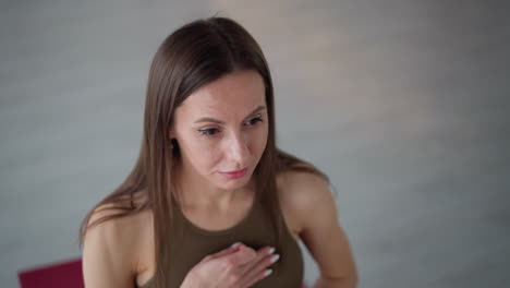 high angle view of mobility instructor meditating on red yoga mat during indoor session with hands resting on chest and stomach in serene bright studio ambiance featuring hanging silk fabrics