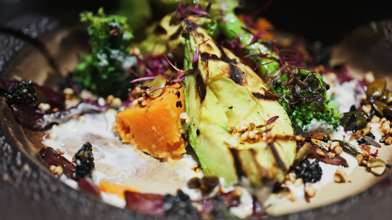 Close up of a woman eating salad with grilled avocado, sweet potato and broccoli on a plate at a restaurant