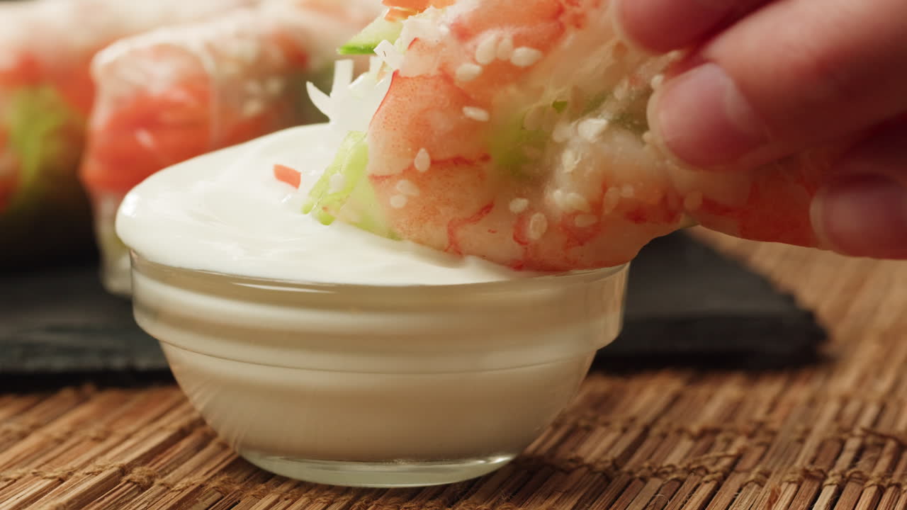 Close-Up of Hand Dipping Fresh Shrimp Spring Roll into Creamy Sauce