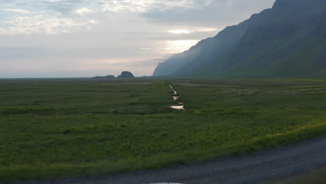 Drone-view-of-amazing-green-highlands-in-Iceland.-Aerial-view-drone-flying-over-stunning-icelandic-landscape-with-river-flowing-and-fog-covering-mountains