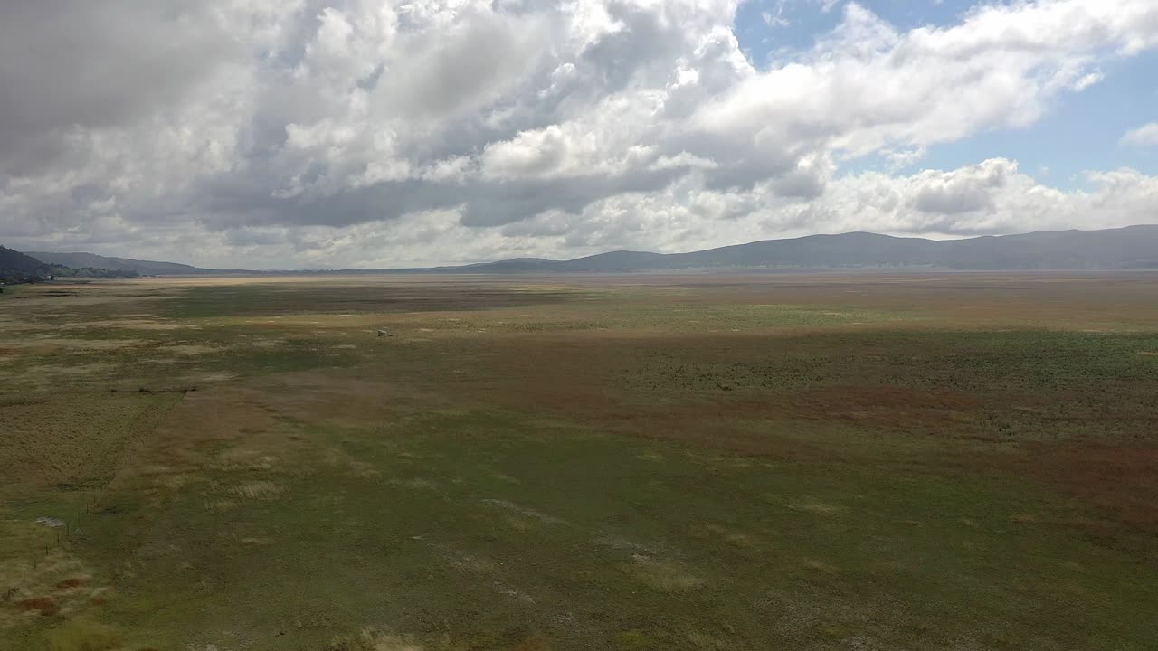 Flyver over tørt landbrugsland, der viser intense brune og grønne nuancer under en stormfuld himmel.