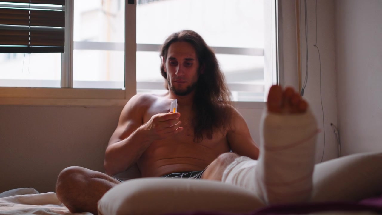 自宅で医療用注射の準備をする、脚にギプスを装着した若い男性。