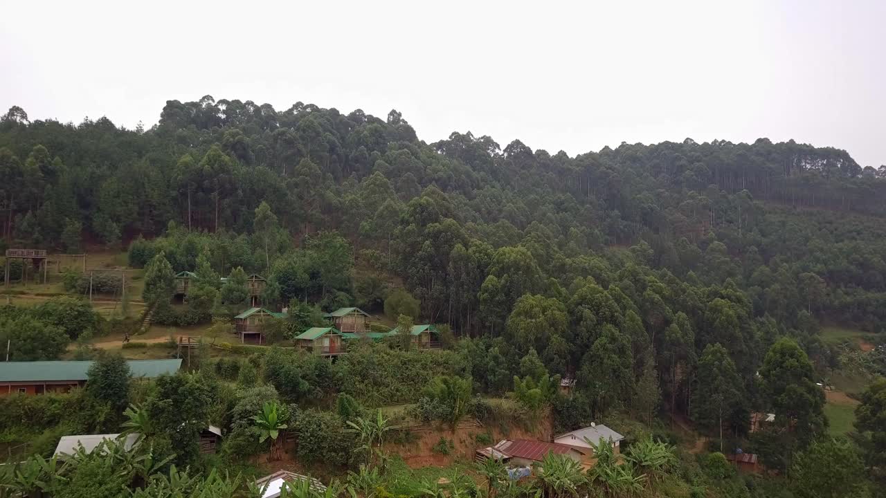 Drone view of tourist accommodation eco lodge in western Uganda, showing forested slopes, scattered lodges, and terraced vegetation in a rural highland setting