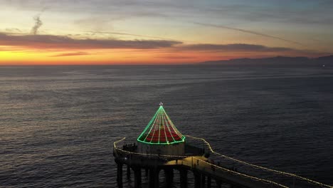 roundhouse aquarium at manhattan beach pier illuminated with lights at sunset - aerial drone shot