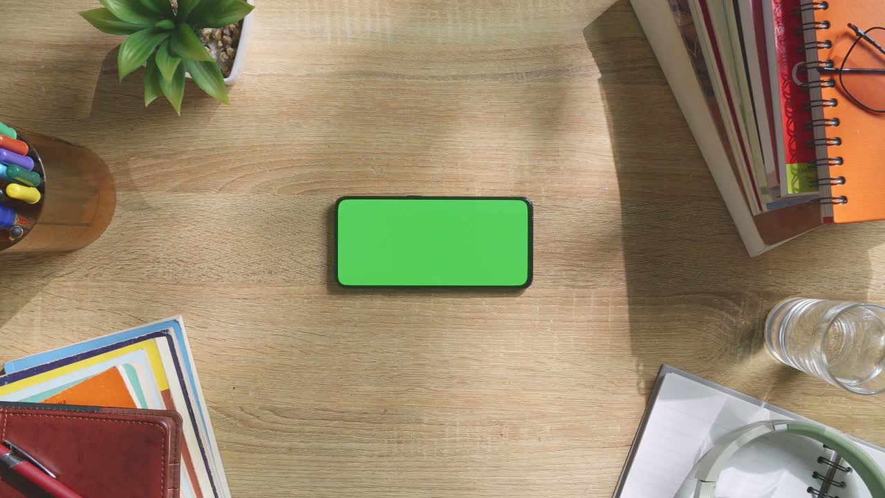 vista de arriba hacia abajo de una computadora portátil con pantalla verde simulada pantalla chromakey en un escritorio de oficina de madera al lado de la libreta con bolígrafos, gafas y un vaso de agua.