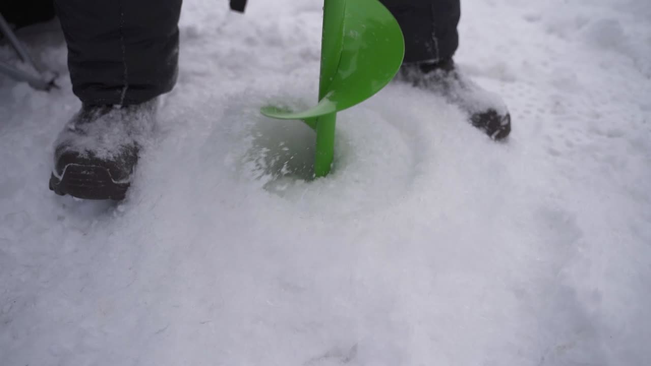오거 드릴을 사용하여 얼음을 시추하는 남자 - 겨울에 소더스 베이에서 얼음 낚시