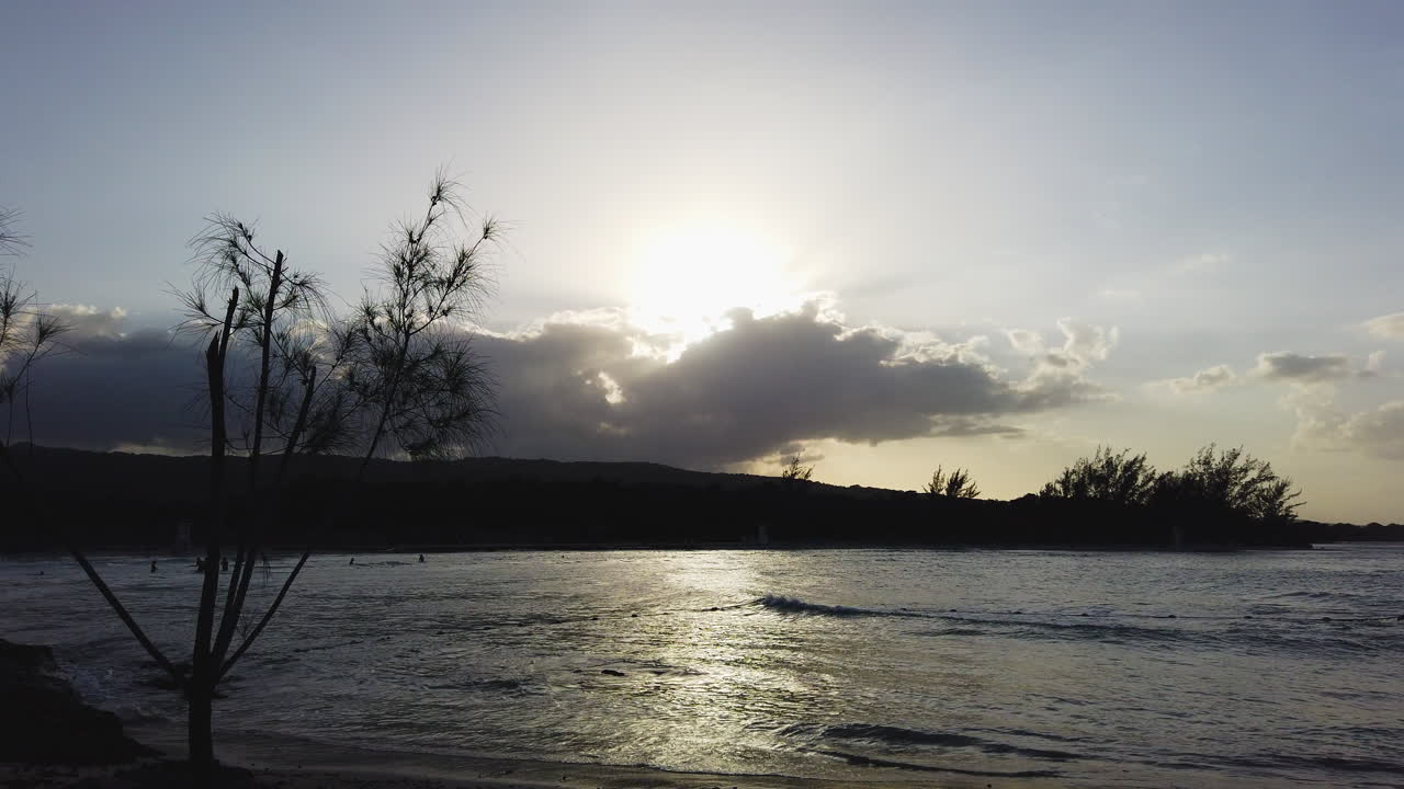 A scenic ocean at sunset in Jamaica with reflections of clouds on the tranquil waters as waves crash gently on ocean