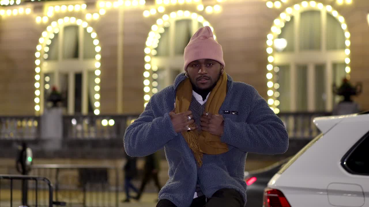 Man posing in front of a brightly lit building at night