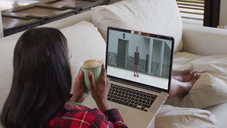 compuesto de una mujer sentada en casa sosteniendo un café viendo un evento de atletismo en una computadora portátil