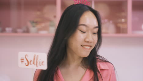 close up view of woman with headdresses and holding cardboard decoration dancing in a pink room celebrating a bachelorette party