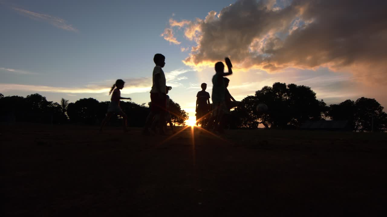Silhouette of children in a clearing in the Amazon rainforest playing soccer during a stunning sunset