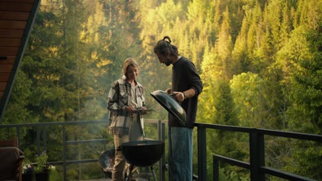 a young couple, a guy and a girl, are relaxing in a country house and frying meat on a special grill against the backdrop of a green coniferous forest