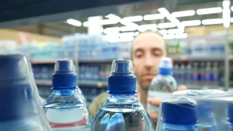 close-up of many bottles of water on a store shelf and a man takes a couple