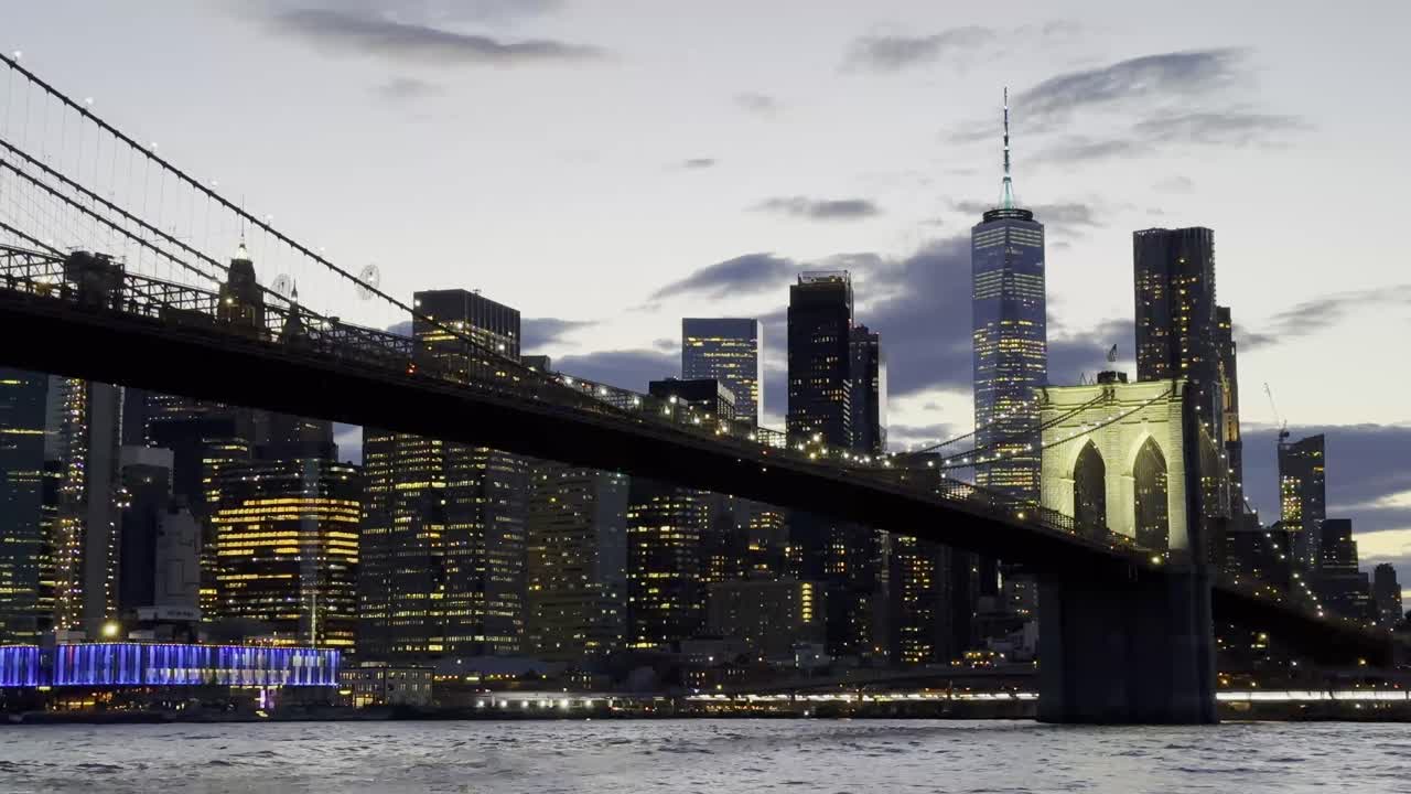 Una vista impresionante del Puente de Brooklyn iluminado por la noche, con las luces vibrantes del horizonte de Manhattan creando un telón de fondo deslumbrante sobre el East River.