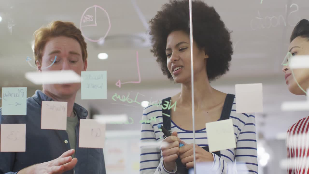 Diverse male and female business colleagues discussing by glass wall with memo notes