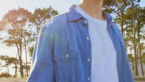 Front-view-of-young-male-skateboarder-walking-with-skateboard-on-country-road-4k