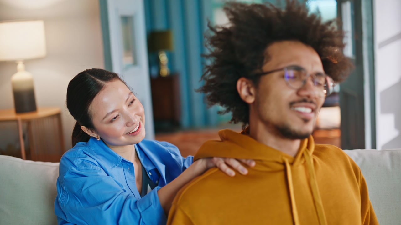Primer plano de pareja multirracial en el sofá. Mujer asiática masajeando los hombros de su novio.