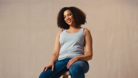 Foto-De-Estudio-De-Una-Mujer-Positiva-Con-Cuerpo-Vestida-Informalmente-Sentada-En-Un-Taburete