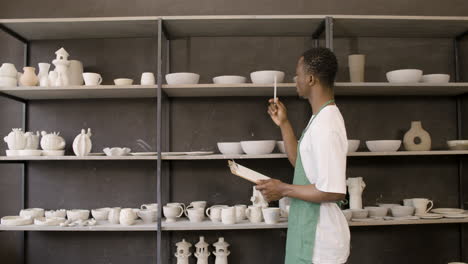 young american male clerk making an inventory of ceramics in the pottery shop