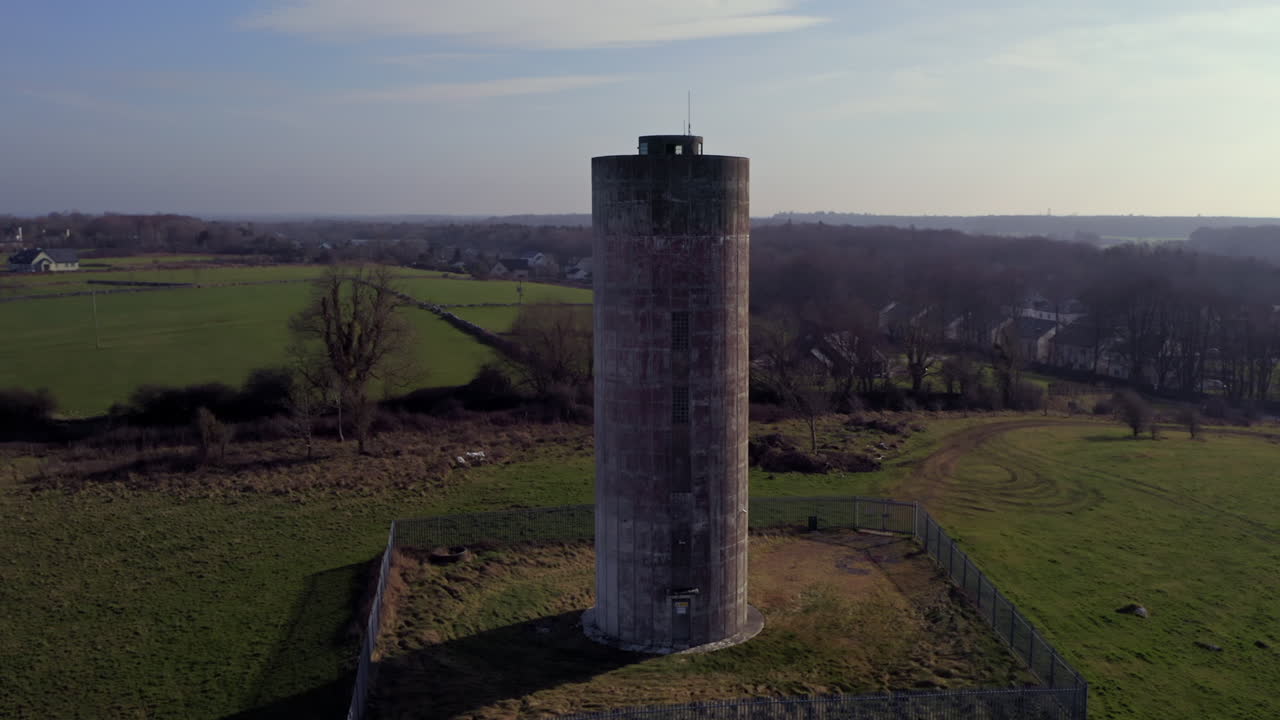 Establishing aerial shot of a cylindrical water tower, well-framed and orbiting to reveal the surrounding Irish landscape