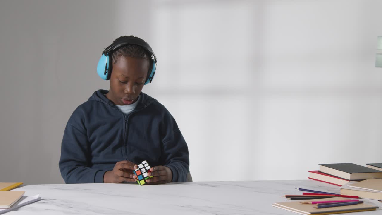 Studio Shot Of Boy On ASD Spectrum Solving Puzzle Cube Wearing Ear Defenders
