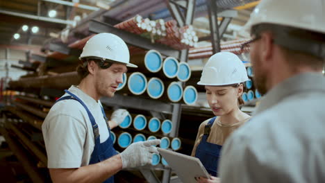 industrial workers inspecting and discussing steel pipes in factory warehouse