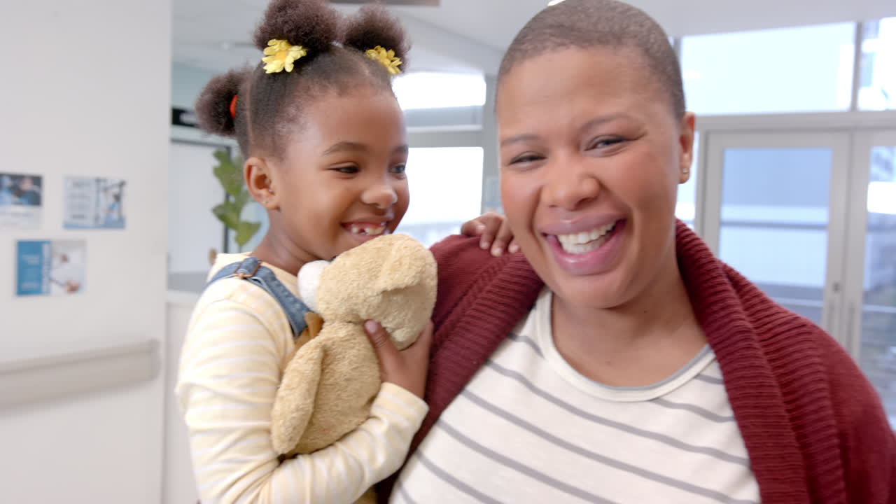 Ritratto di madre afroamericana felice che tiene in braccio la figlia con una mascotte in ospedale, al rallentatore.