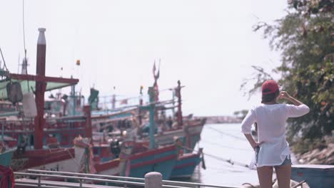 young lady in shirt looks at asian fishing boats from coast