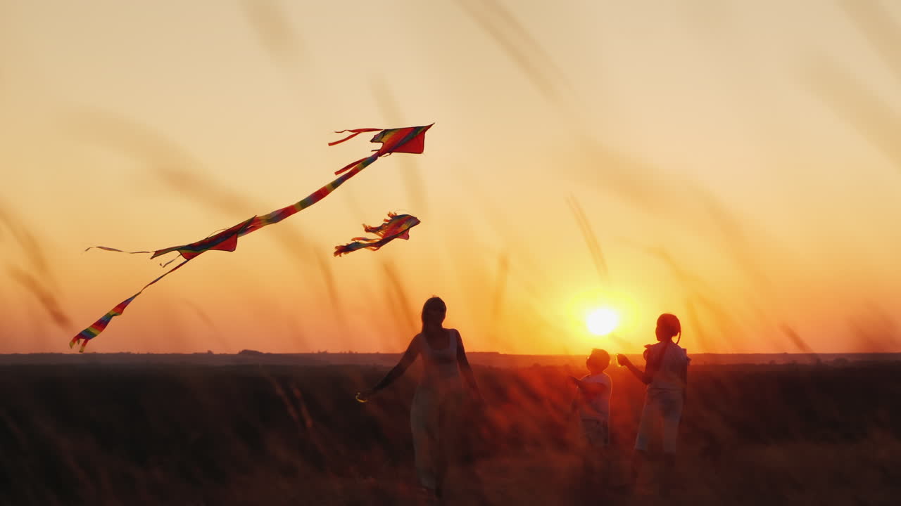 una mujer activa y sana de mediana edad juega con dos niños cometas al atardecer concepto de vacaciones de verano