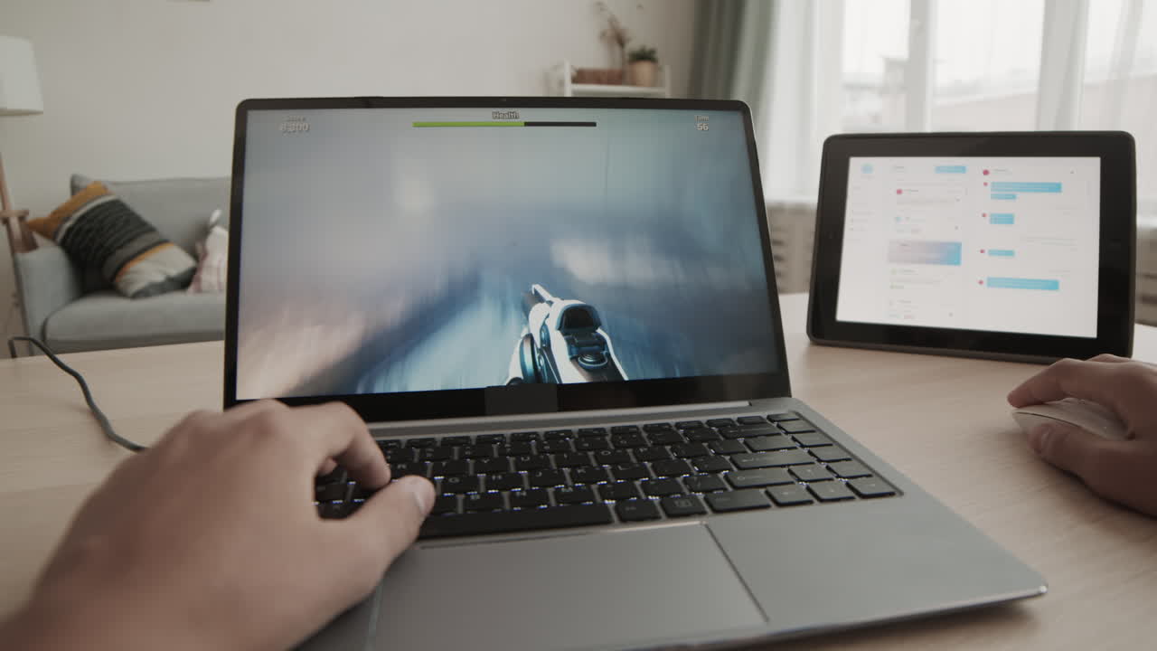 Person playing a video game on a laptop with a tablet next to it