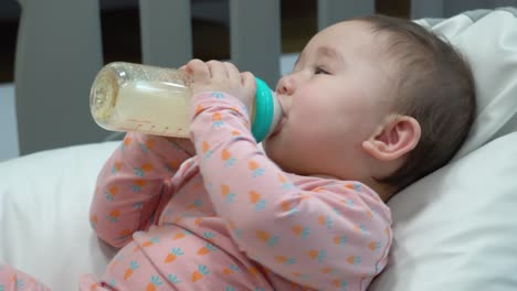 pequeño bebé caucásico bebiendo leche de fórmula sosteniendo una botella sola con las dos manos