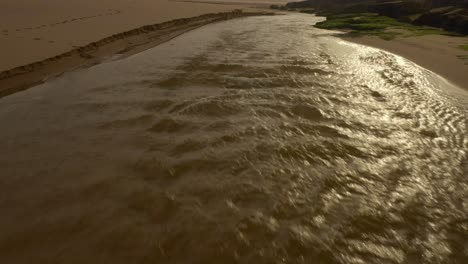 river flowing at beach in portugal, early morning golden cliffs