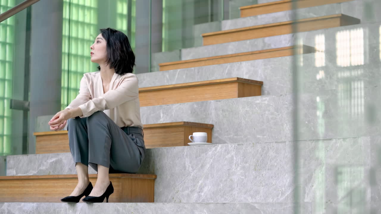Affascinante donna manager che si sta concedendo un momento di relax sulle scale, apparendo pensierosa e rilassata, in un contesto d'ufficio elegante. La professionista sicura di sé si gode una breve pausa dal lavoro.