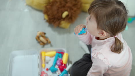 age 3 girl with pigtails playing doctor using toy plastic tools to check examine neck tonsils