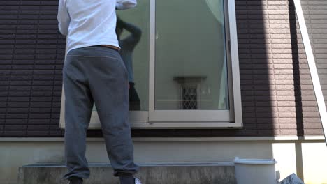 a man cleaning the exterior of a glass window of his home - mid shot