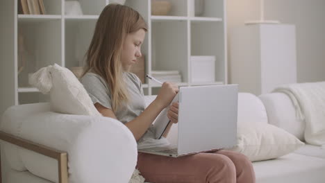 adolescente está viendo entrenamiento en línea por computadora portátil desde casa y aprendiendo a distancia escribiendo notas en el cuaderno relajarse y atmósfera doméstica