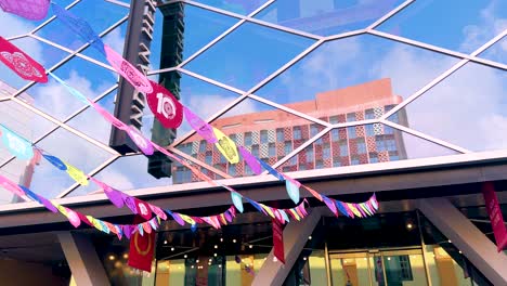 vibrant paper flags flutter in the wind above a modern outdoor plaza in singapore, captured with upward camera movement and bright daylight