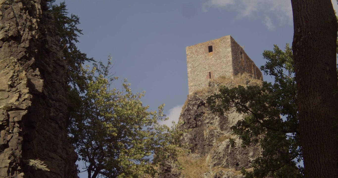 Un'inquadratura dal basso della storica torre del Castello di Trosky arroccata su una formazione rocciosa vulcanica, circondata da alberi verdi lussureggianti nella regione del Paradiso Boemo