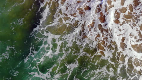 Roiling-Pacific-Ocean-surf-2-and-waves-from-directly-above,-tracking-with-4k-drone-at-Huntington-Beach,-Southern-California-onto-sand