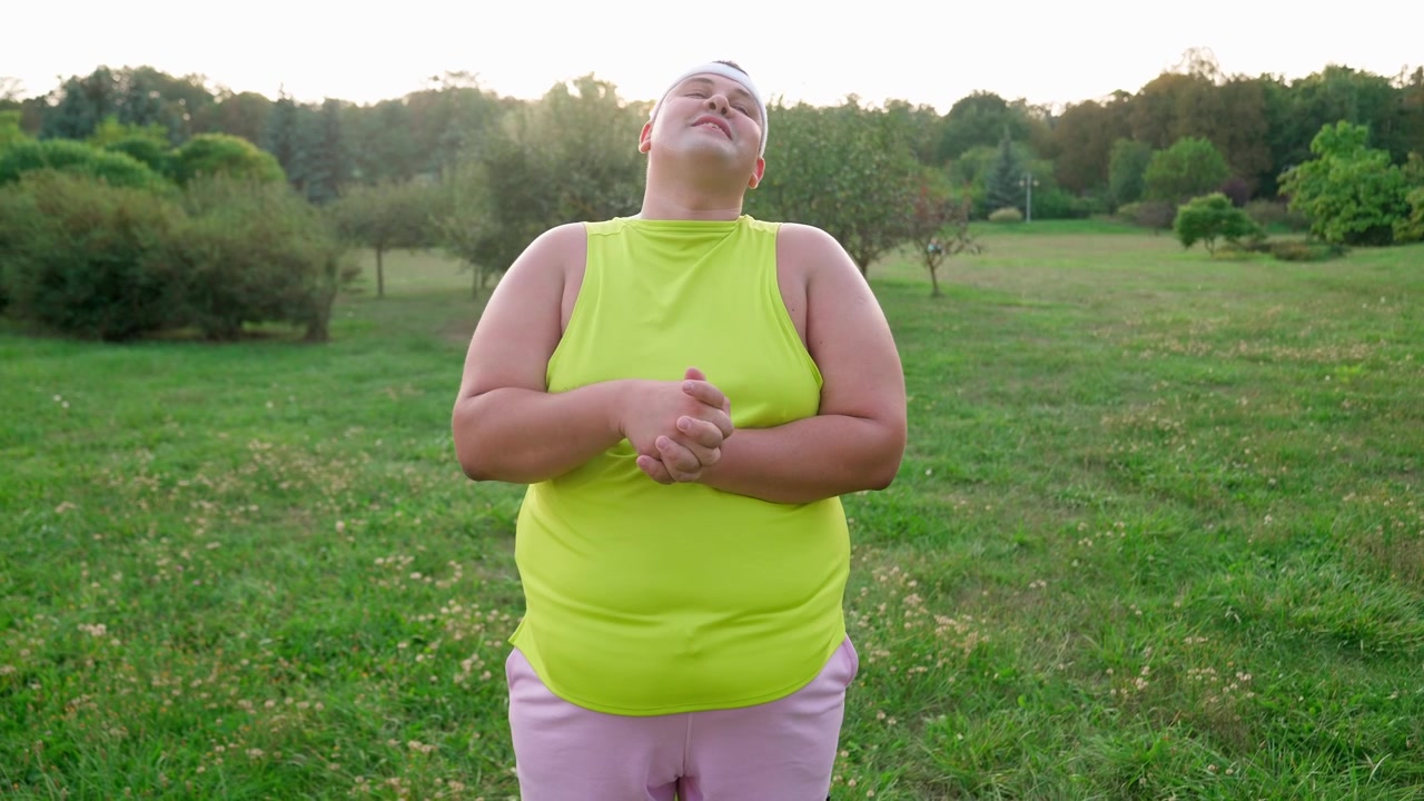 Uomo in sovrappeso felice che fa stretching al collo al parco