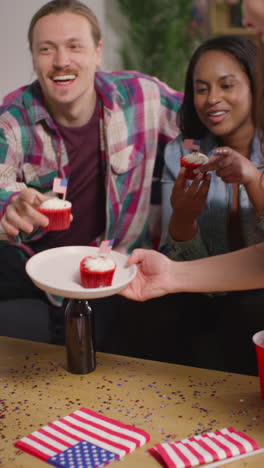 video vertical de una mujer en casa sirviendo pasteles con estrellas y rayas americanas en miniatura banderas a amigos en una fiesta que celebra el 4 de julio, día de la independencia 1