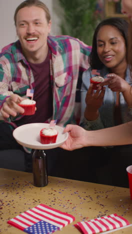 vertikales video einer frau zu hause, die cupcakes mit miniaturisierten amerikanischen sternen und streifen und flaggen für freunde auf einer party zur feier des 4. juli, dem tag der unabhängigkeit, serviert.