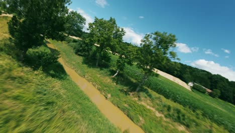 a drone flies over a field of crops, passing by a bridge and a small forest