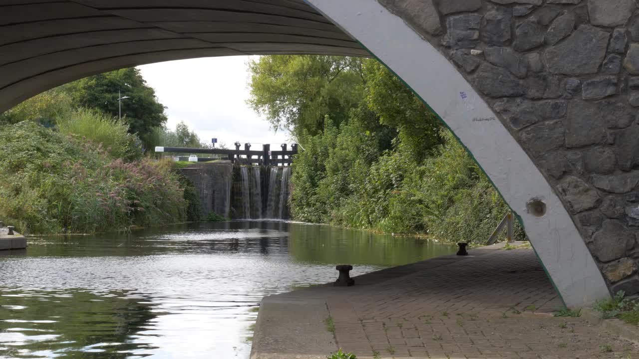 hermosa vista bajo un pequeño puente antiguo con agua de río que fluye a través de la antigua compuerta del canal en un hermoso día de verano en dublín, irlanda
