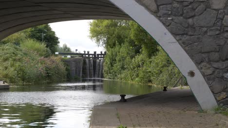 Beautiful-View-Under-A-Small-Old-Bridge-With-River-Water-Flowing-Through-Old-Canal-Sluice-Gate-On-Lovely-Summer-Day-In-Dublin,-Ireland