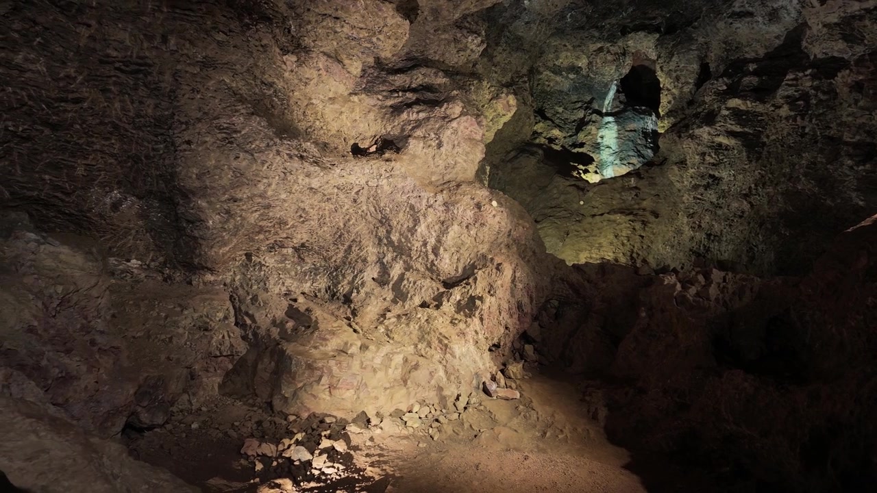 Rough rock walls of a Clearwell Caves chamber are picked out by spotlights, revealing textures and a rubble-strewn floor.